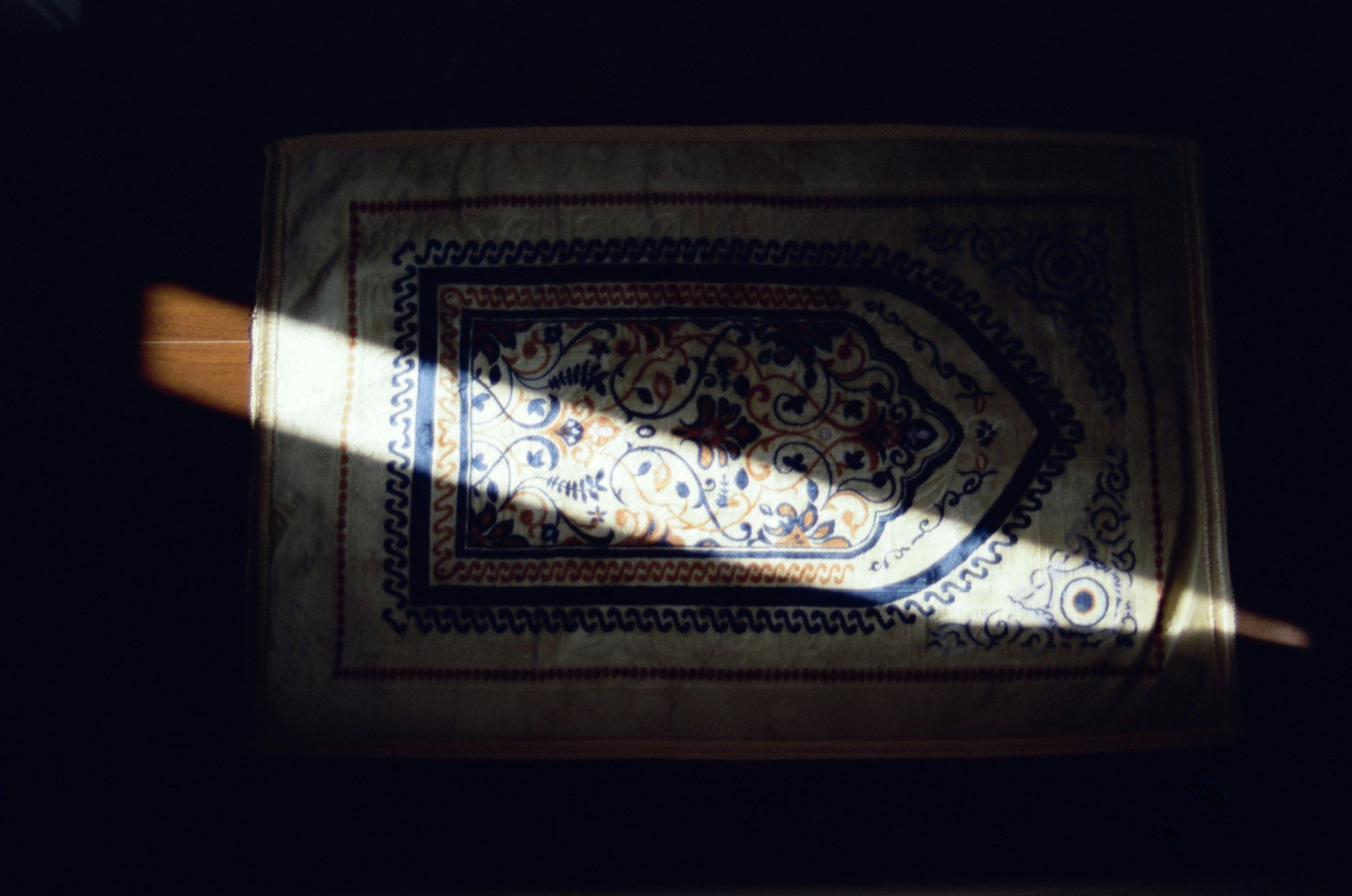 A prayer mat in a shaft of light in a dark room.